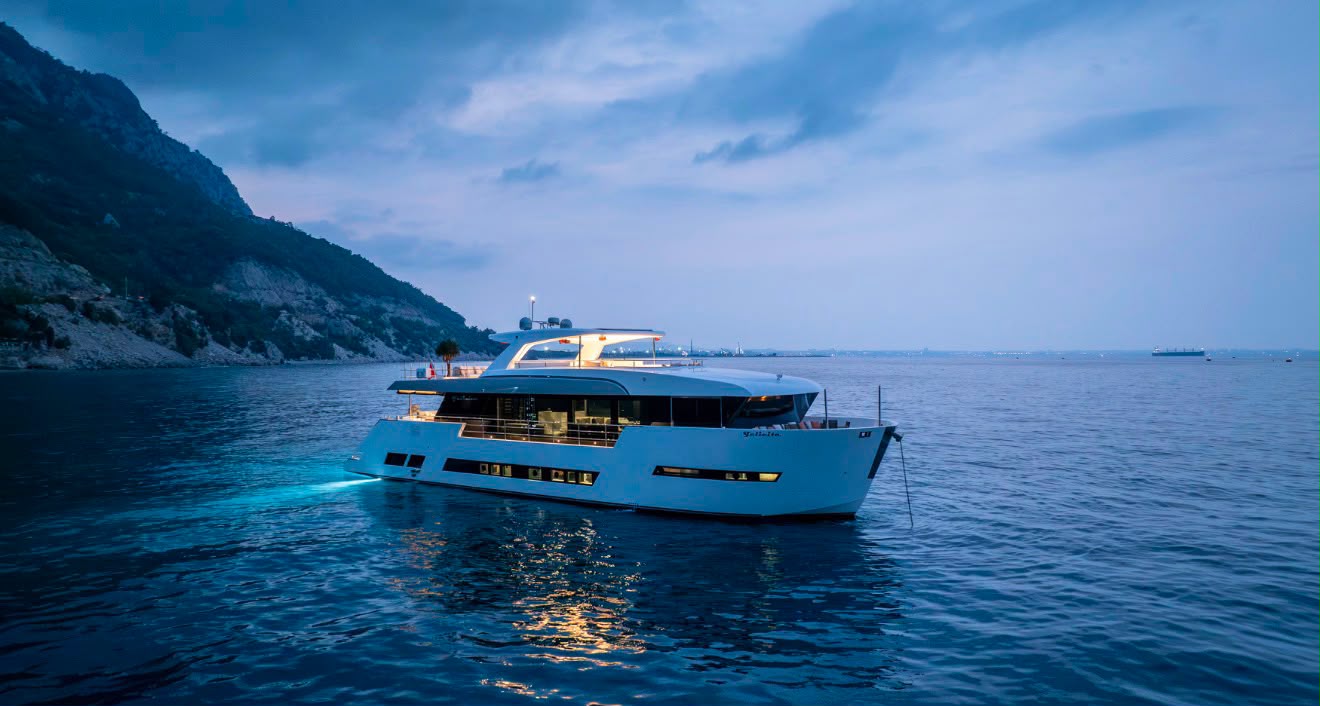 Felicita under way at twilight, underwater lights glowing at the stern